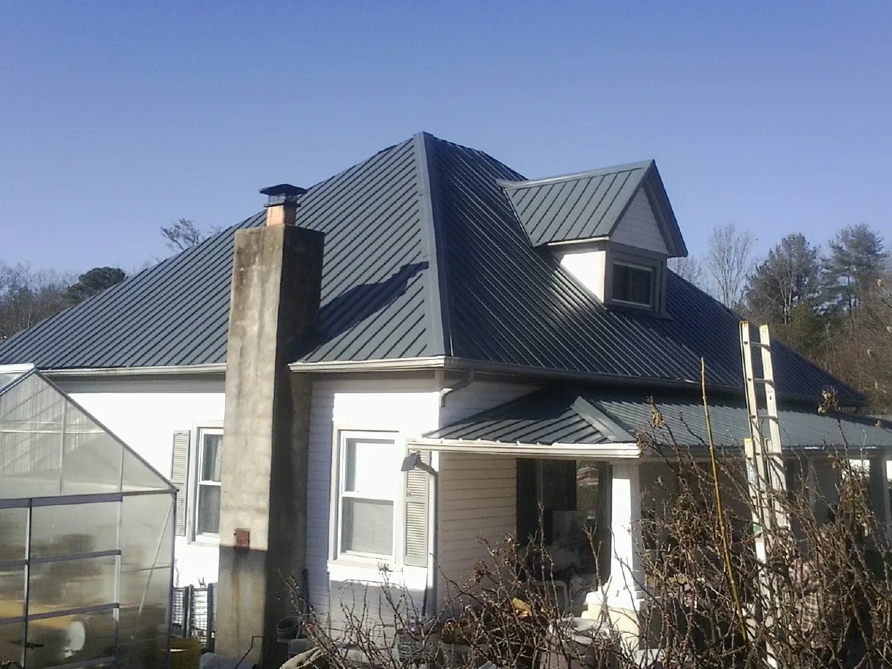Dark blue standing seam metal roof on a white farmhouse with dormer — Slate & Tile Roof Repair by Roofing Brothers in Rush
