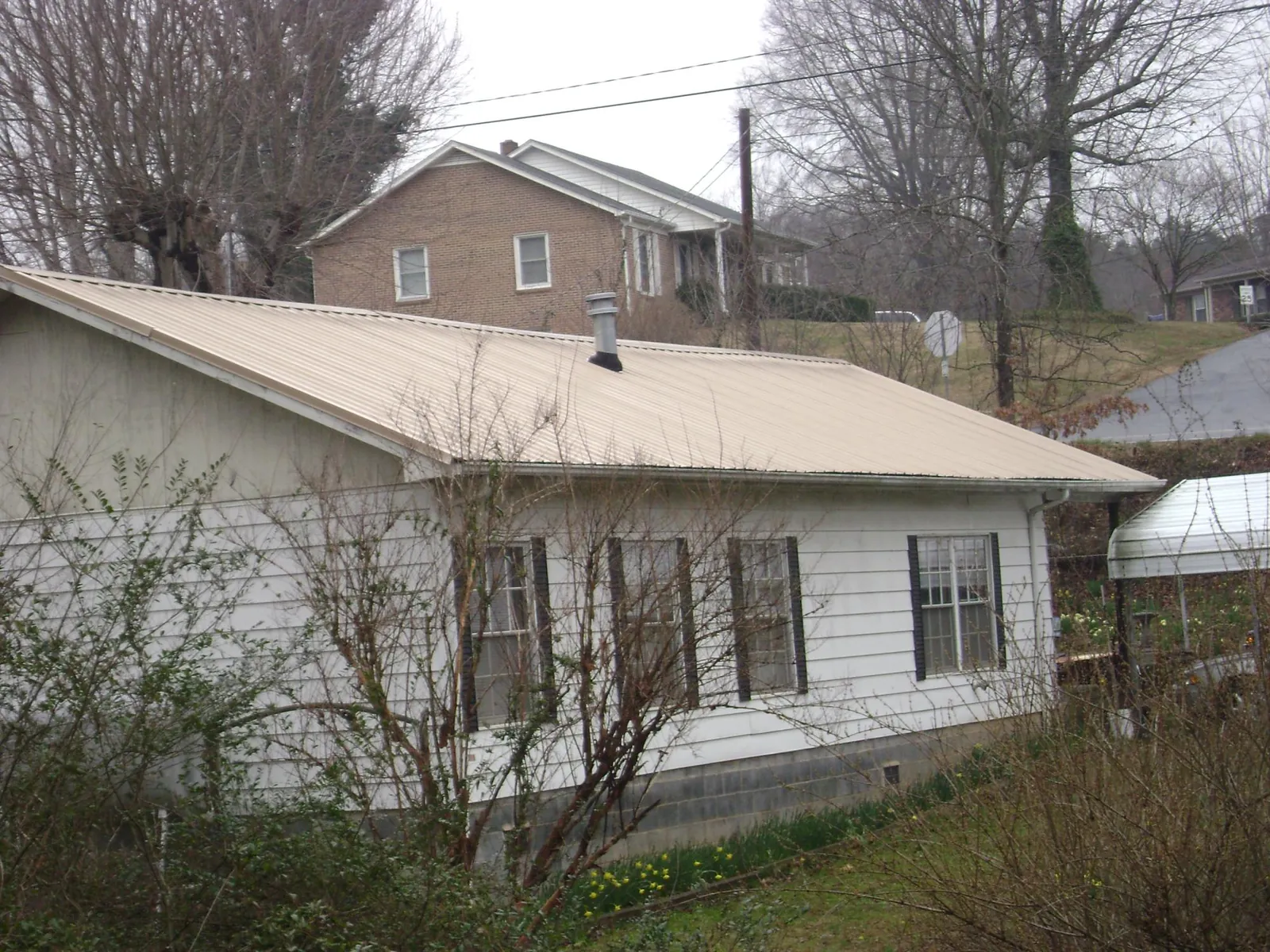 Tan metal roof on a white sided house set into a hillside — Commercial Roofing by Roofing Brothers in Rush