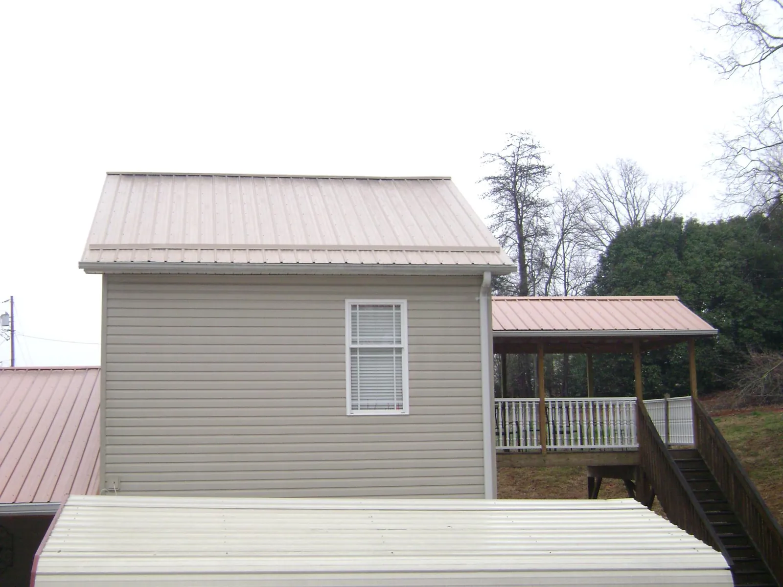 Tan metal roofs on a two story addition and attached porch, from a Roof Replacement job in Rush